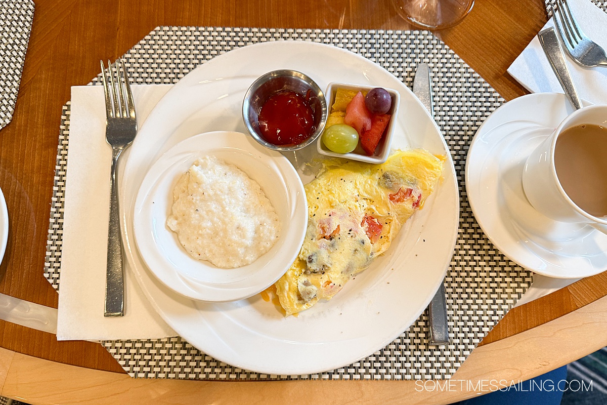 Breakfast plate with grits in a small dish on the left, an omelet on the right and fruit and ketchup above it in small containers.