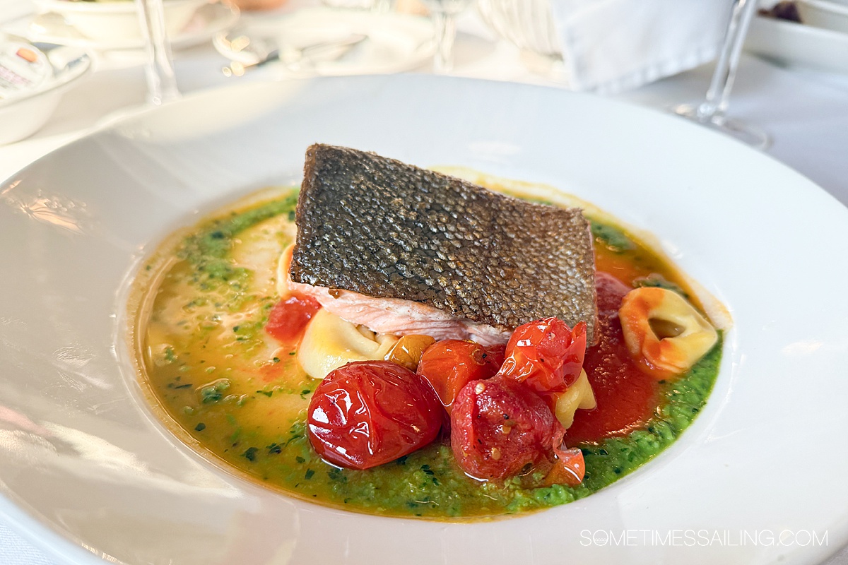 Trout on a plate with a bed of tomatoes and pesto sauce surrounding it.