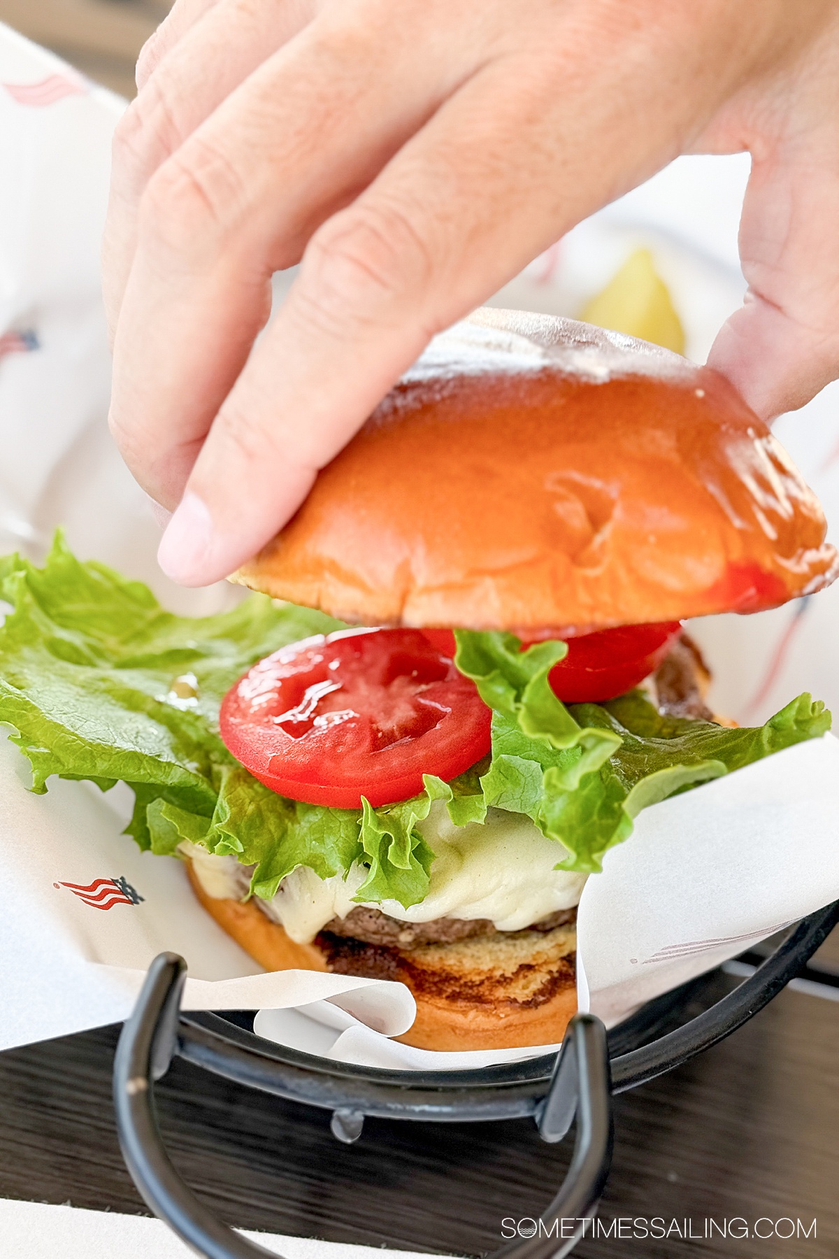 Hand putting a bun on top of a hamburger with lettuce and tomato.