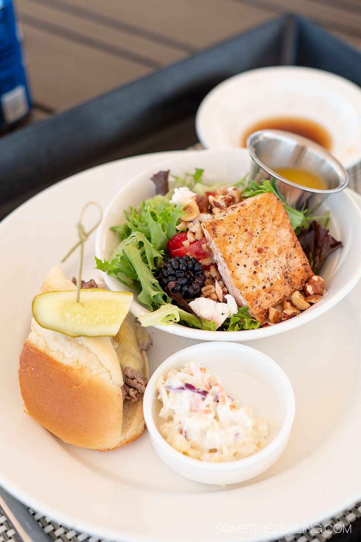 Half a salad in a bowl with a slider on the side with a pickle topper and a small bowl of cole slaw.