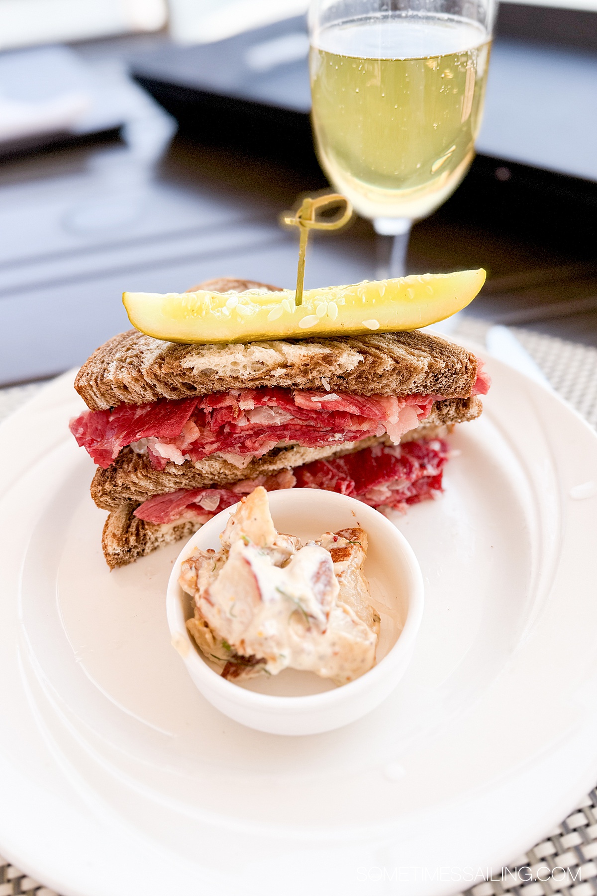 Half a Reuben sandwich on a plate with a small dish of potato salad.