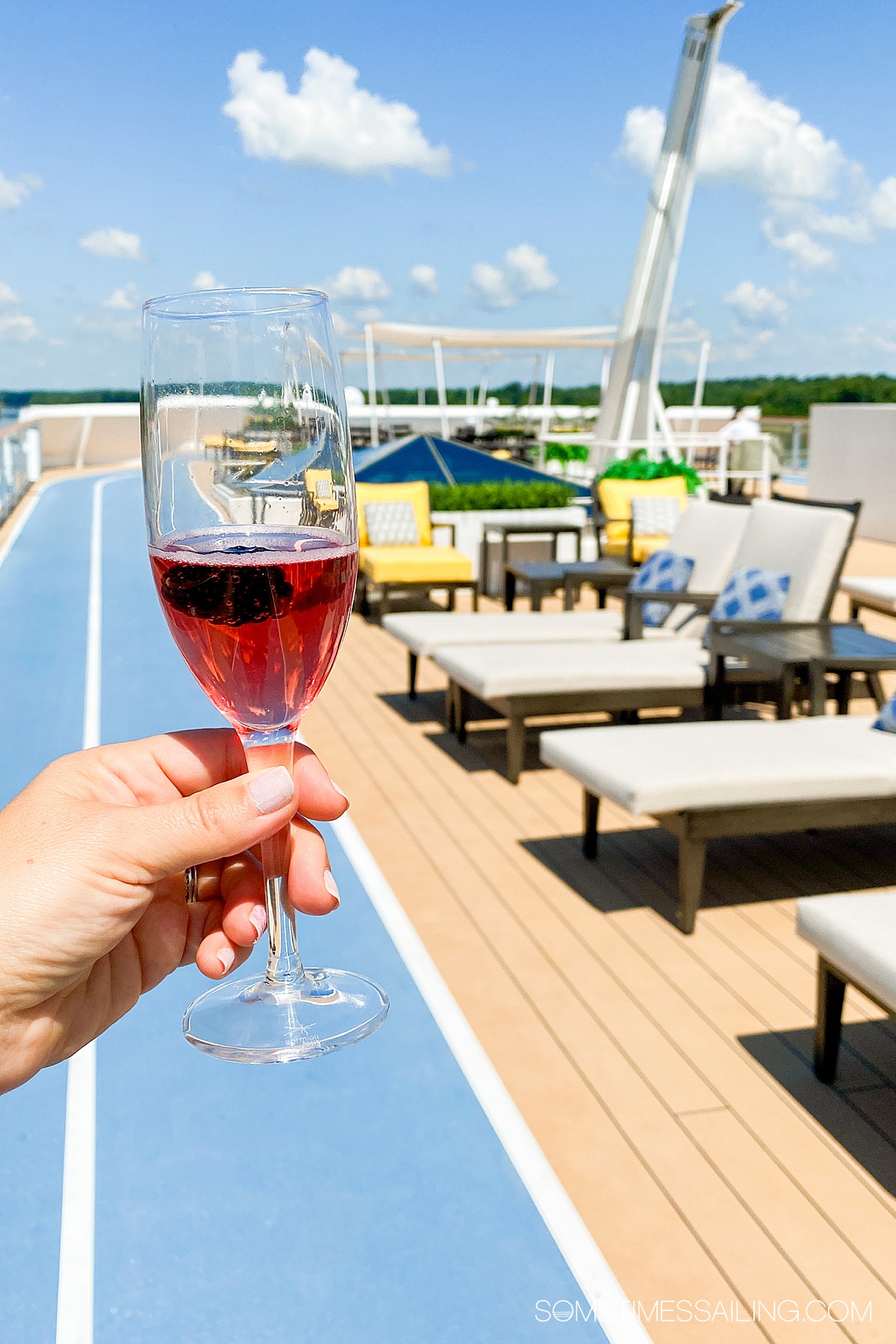 Hand holding a glass of red wine on a top deck on a sunny, blue-sky day.
