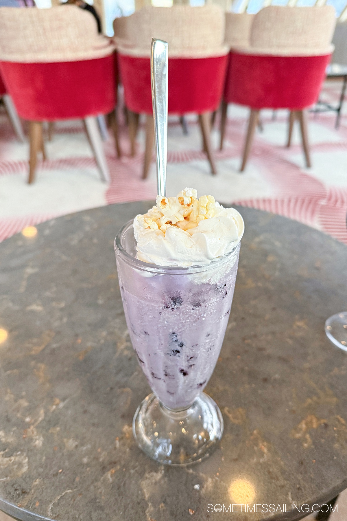 A dish of purple huckleberry ice cream in a tall glass with whipped cream and a popcorn on top.