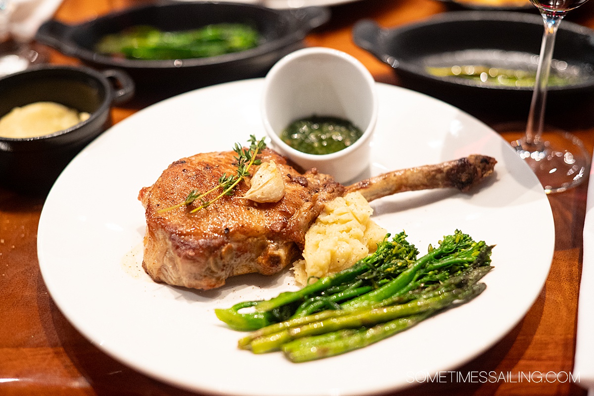 Plate with a bone-in pork chop, broccolini, mashed potatoes.