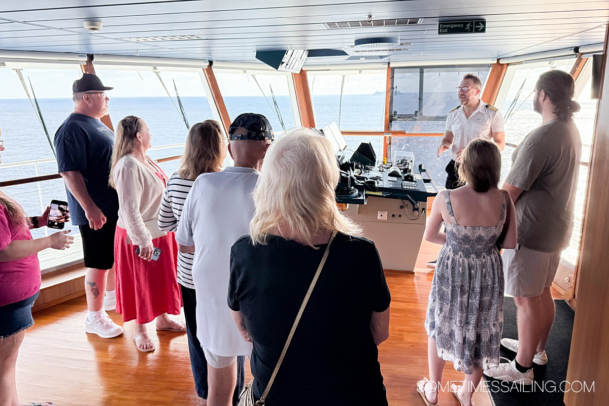 People in the bridge of a cruise ship with the captain in the background talking to them.