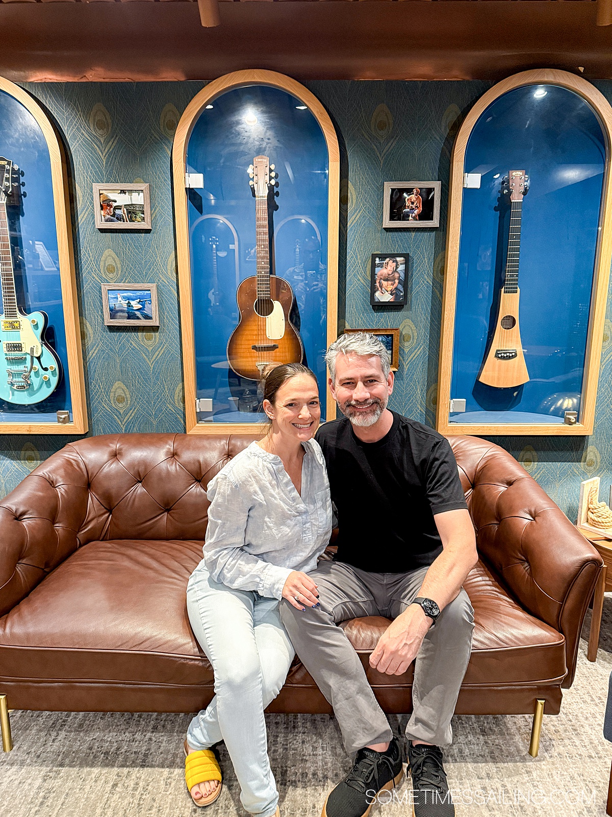Couple on the couch in front of guitars in frames on the wall.