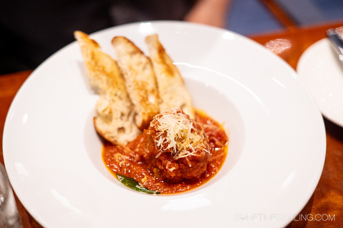 Plated meatball with three slices of toasted bread on the side topped by grated parmesan cheese.