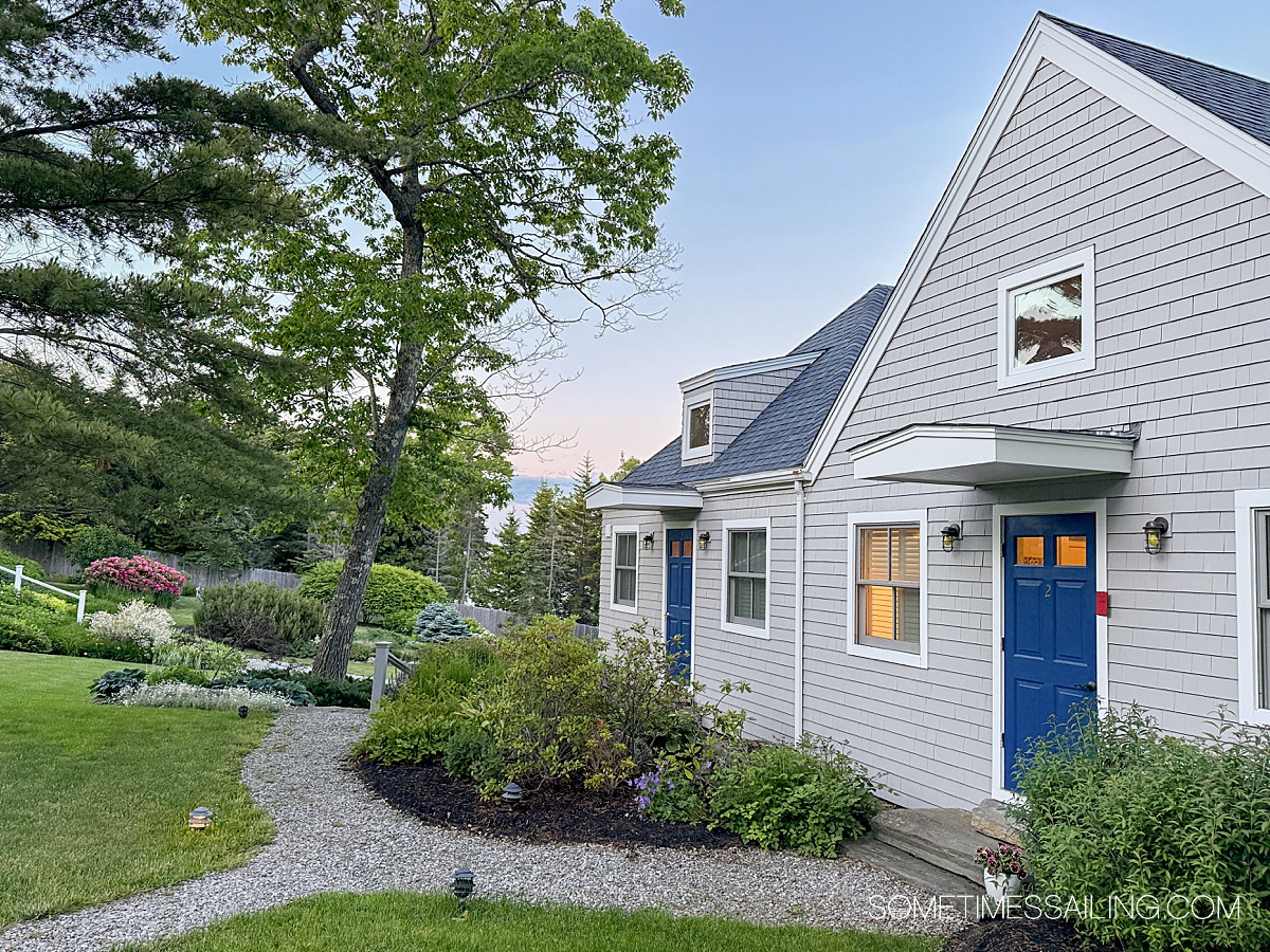 House with gray siding and a blue door and landscaping surrounding it in Maine.