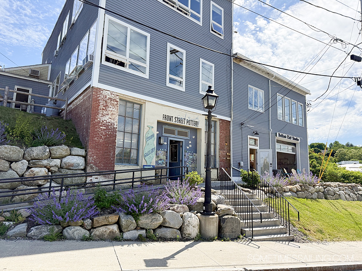 Gray building with two shops and a ramp up along the road in Belfast, Maine.