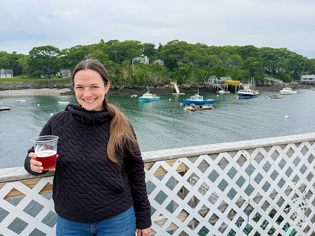 Woman in front of a waterfront harbor, holding a beer.