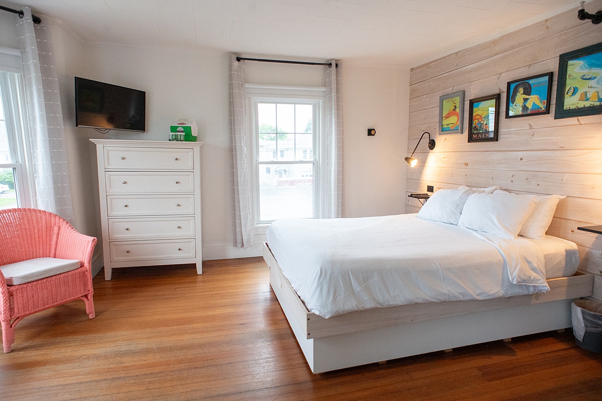Interior of a hotel room with white linens on a queen bed and wood floors.