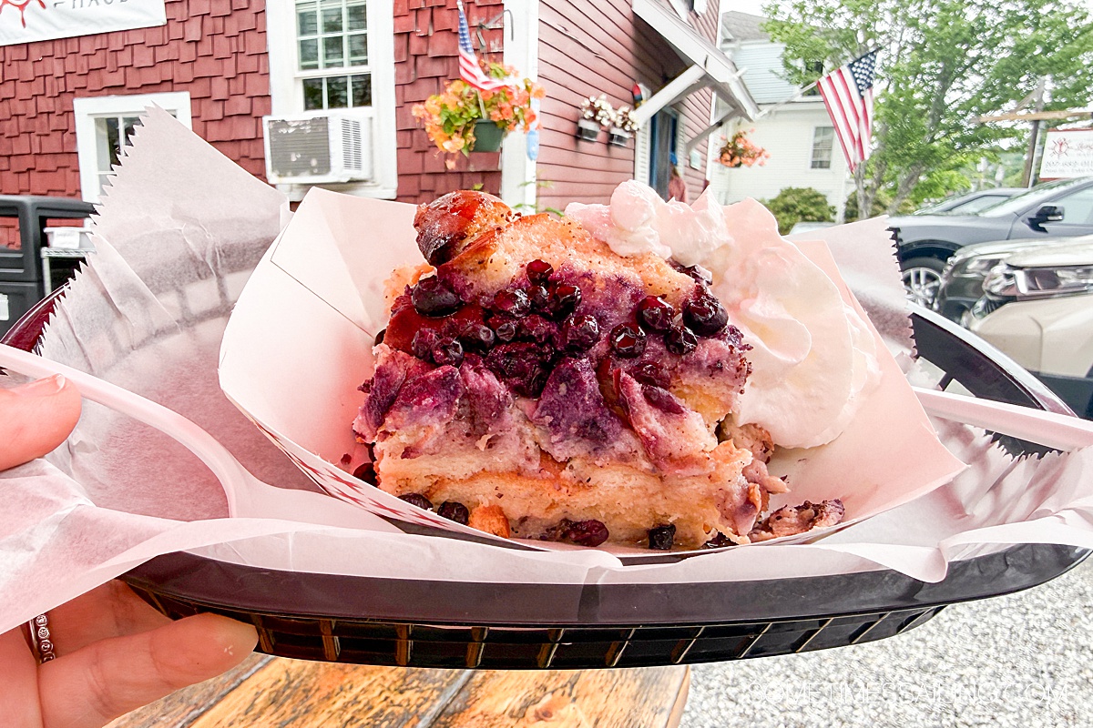 Black basket with a thin piece of paper and a square of bread pudding with blueberries on top.