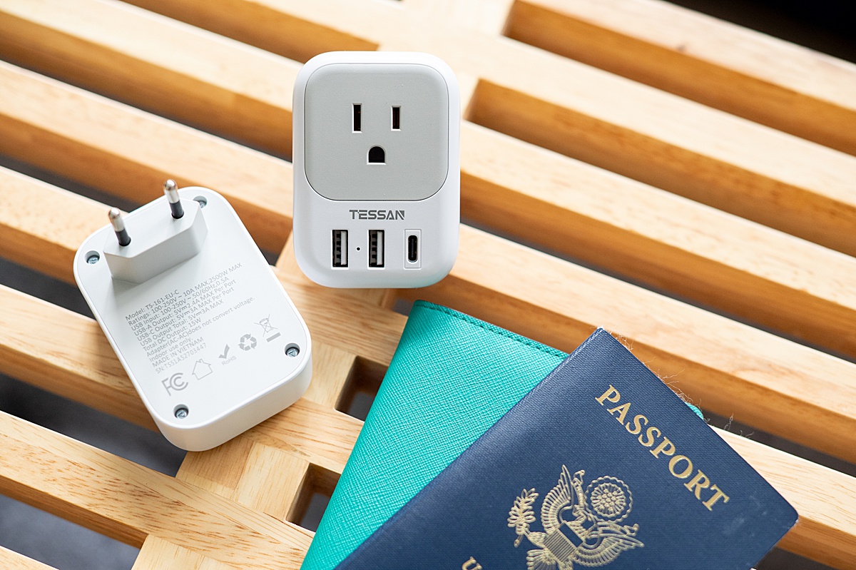 Travel adapters sitting on a wooden bench next to a passport.