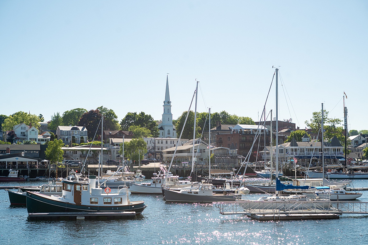 View of a boat-filled harbor in front of the land with a church and other buildings in Camden, Maine.
