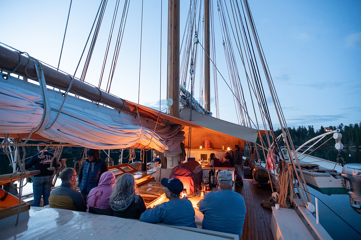 Guests on the top deck of a schooner with the sails down during dusk.