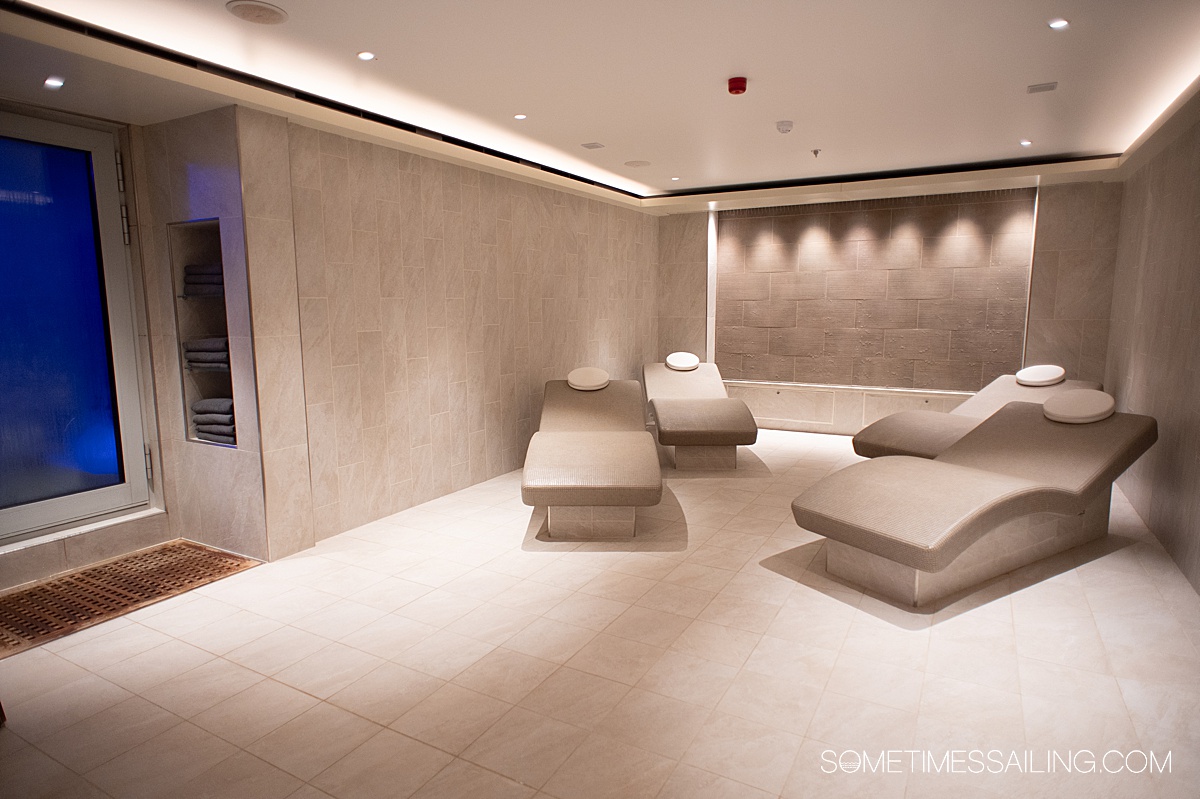 Four tiled heated chairs in the distance inside a tan-colored spa room.