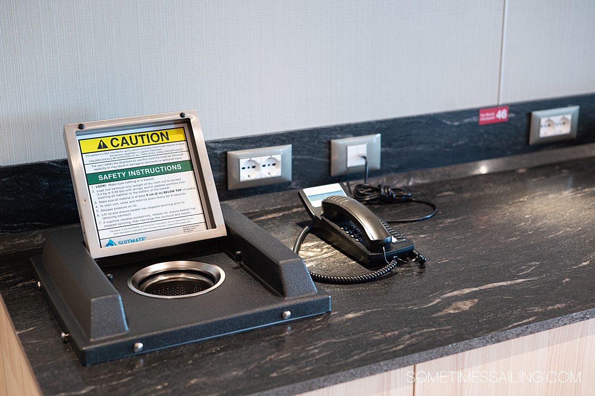 Counter space with a phone and a silver dryer drum to dry a bathing suit.
