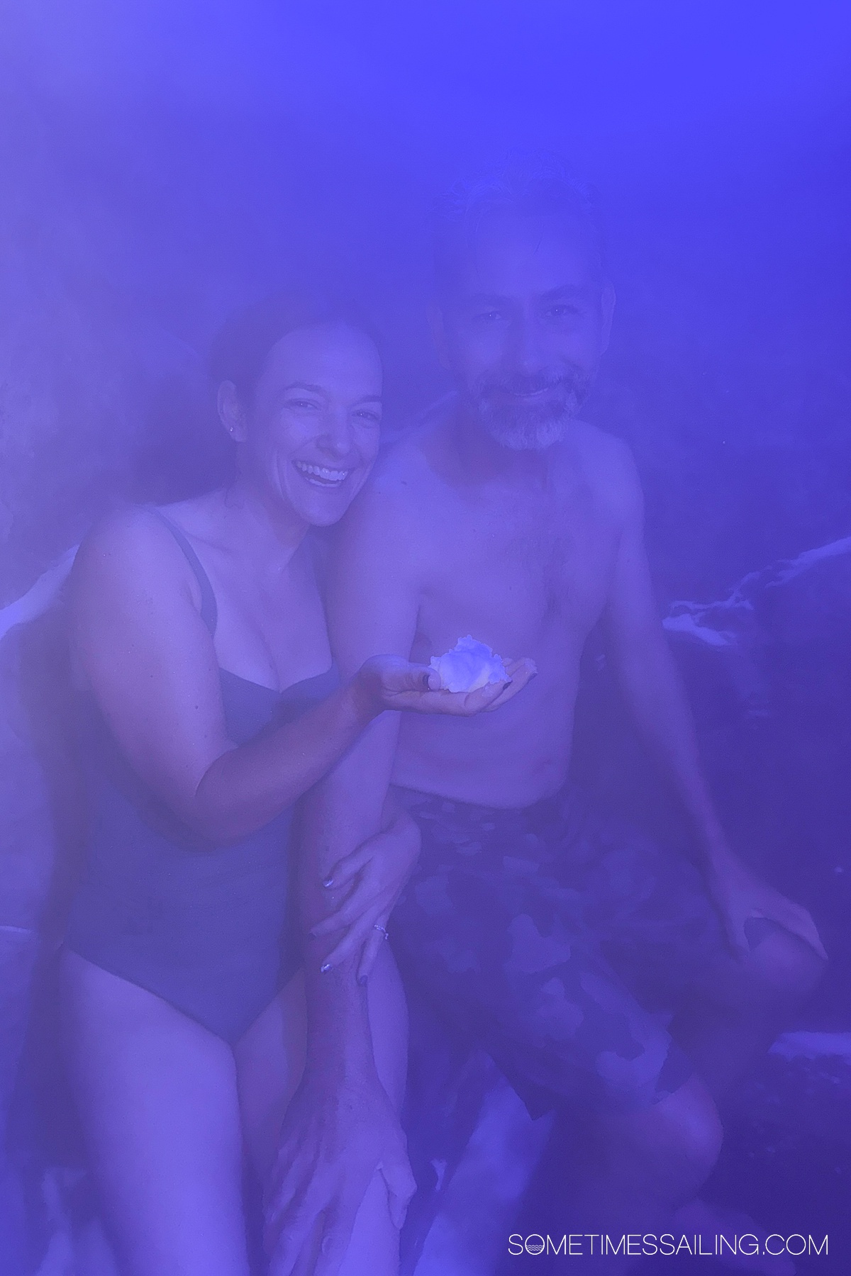 Couple under purple lights in bathing suits holding a snowball.